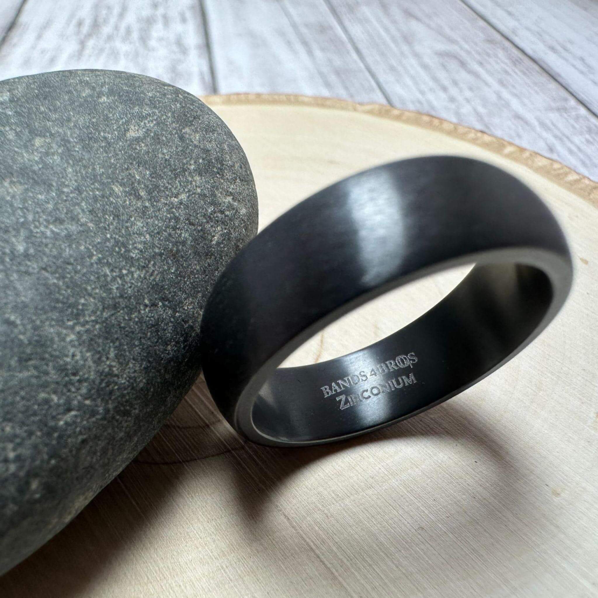 Black Zirconium Men's Wedding Band with Dome Design Against Gray Rock with Focus on the Engraving | The Electron